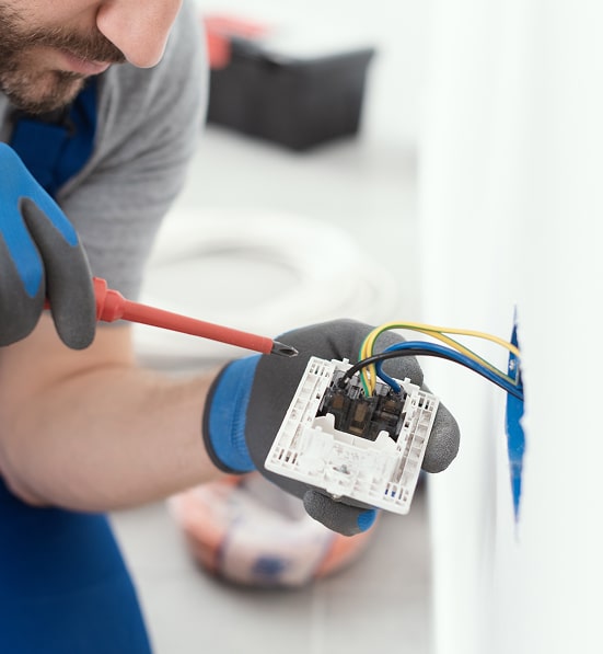 Électricien : installation et câblage électrique sécurisé. Électricien effectuant le câblage d'un interrupteur ou d'une prise. Il utilise un tournevis isolé sur les fils (terre, neutre, phase) avec des gants.