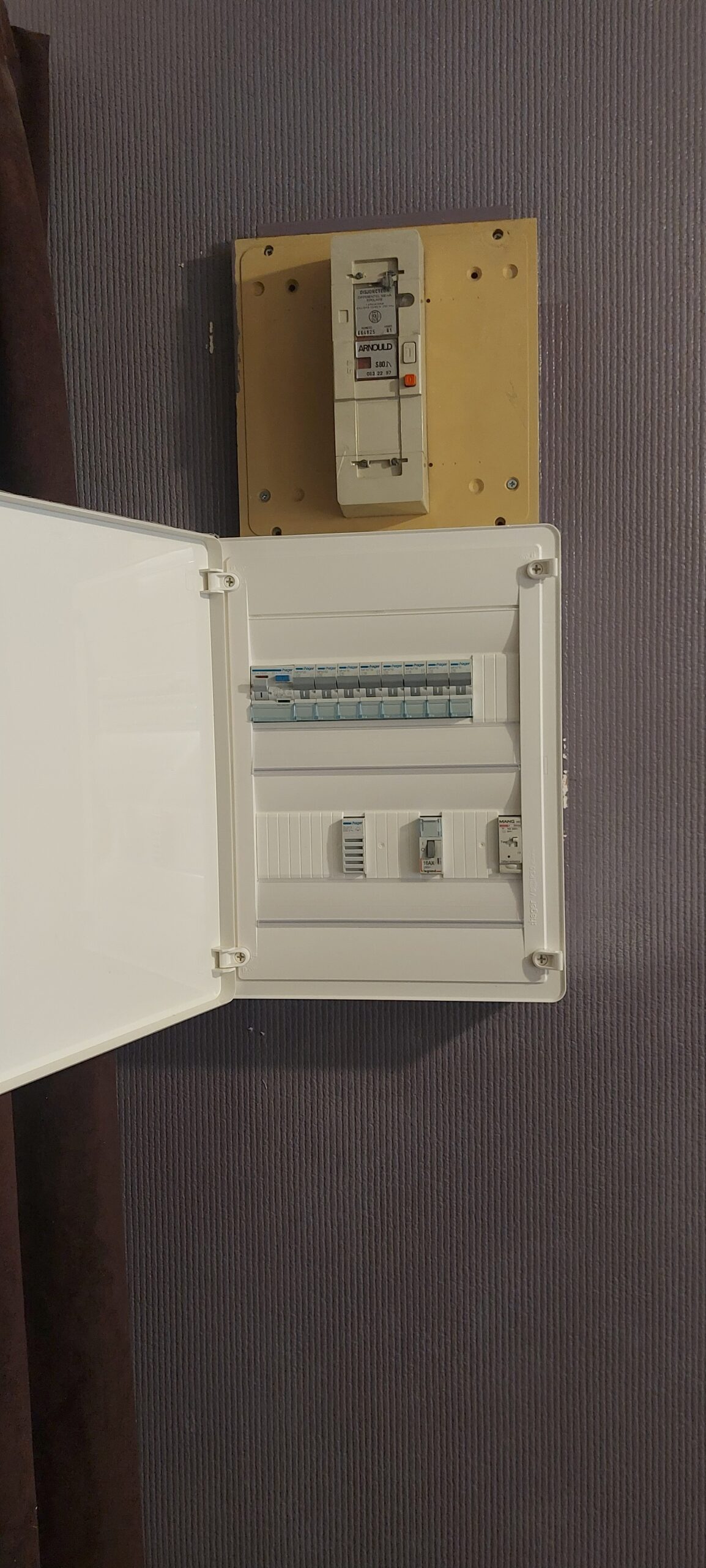 Tableau électrique blanc ouvert avec disjoncteurs Hager et ancien disjoncteur Arnould sur mur violet texturé.