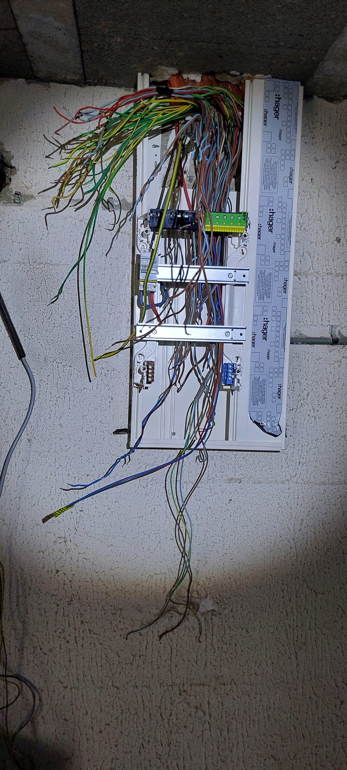 Tableau électrique Hager ouvert avec fils en désordre, câblage électrique complexe sur mur en crépi.