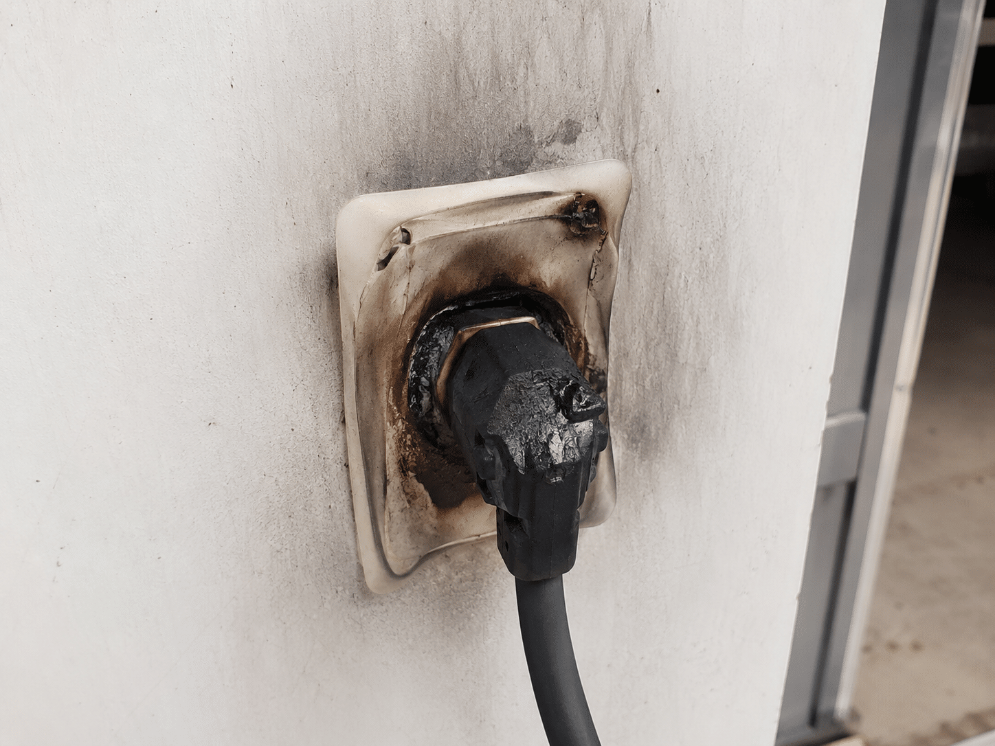 Prise électrique brûlée et fondue avec suie sur mur blanc.